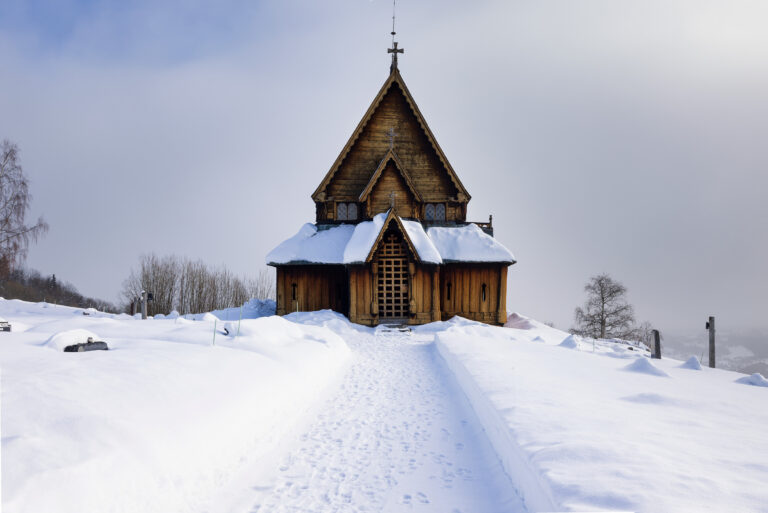 Reinli stavkirke sett forfra, i snødekket landskap med delvis skyet himmel i bakgrunnen.